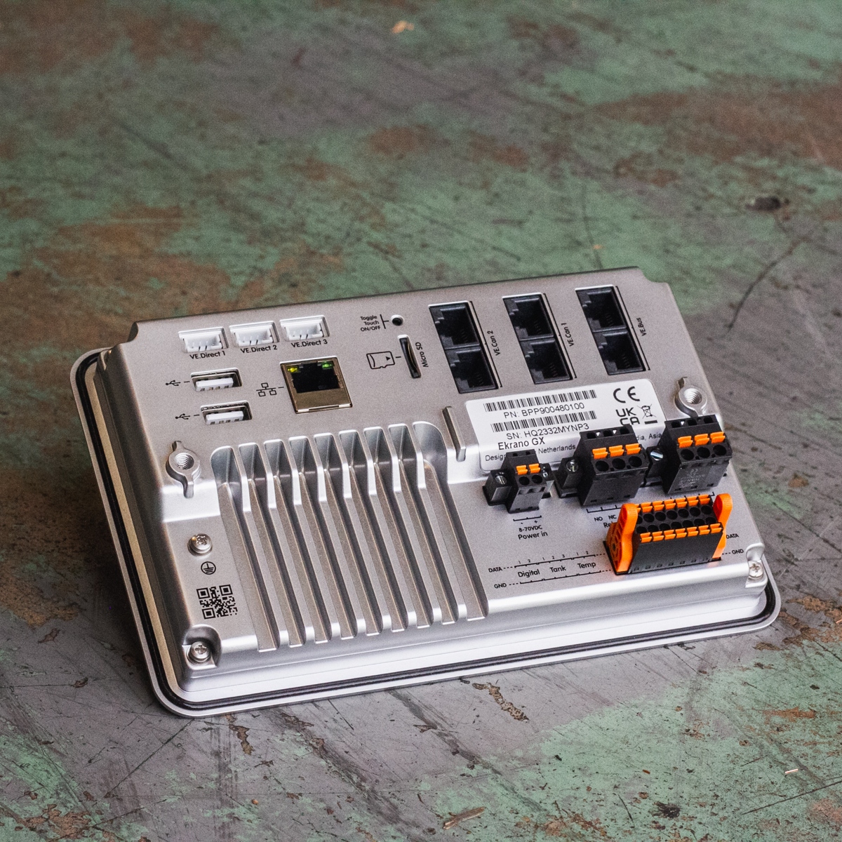 A sleek metal electronic device, the Victron Ekrano GX Monitoring System, equipped with multiple ports including USB, Ethernet, and connectors, elegantly positioned on a worn surface.