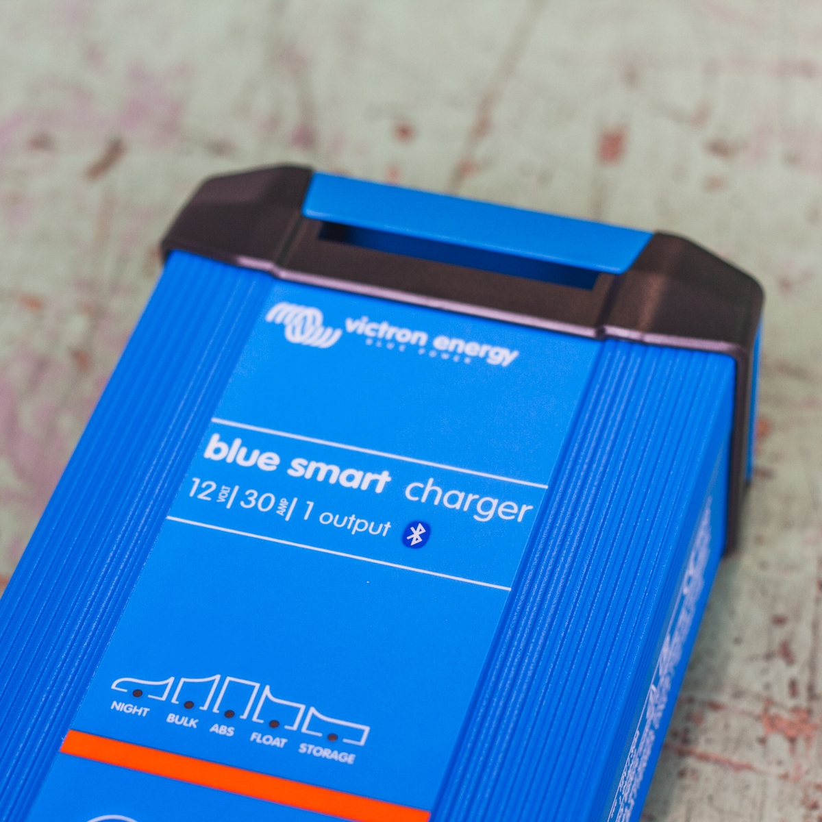 A Victron Battery Charger 12/30 - Indoor (IP22) Blue Smart - 1 Output with Bluetooth capability, in a blue color, rests on a light-colored surface.