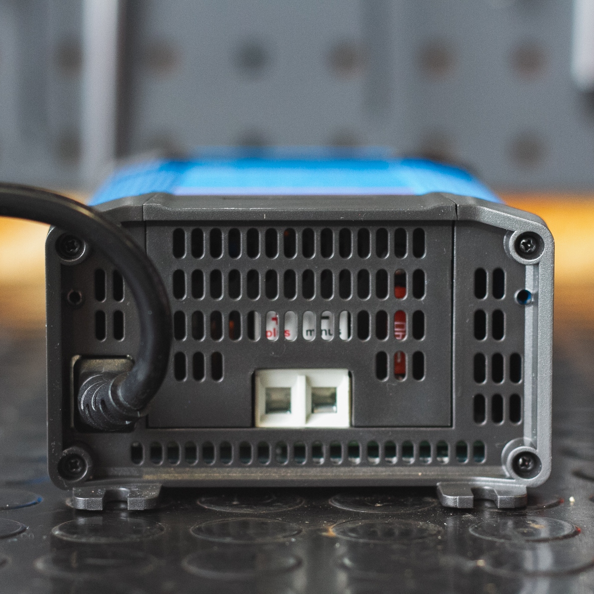 A close-up of a black electronic device, possibly the Victron Battery Charger 12/30 - Indoor (IP22) Blue Smart - 1 Output, with a vented rear panel and connected cables on a black mat.