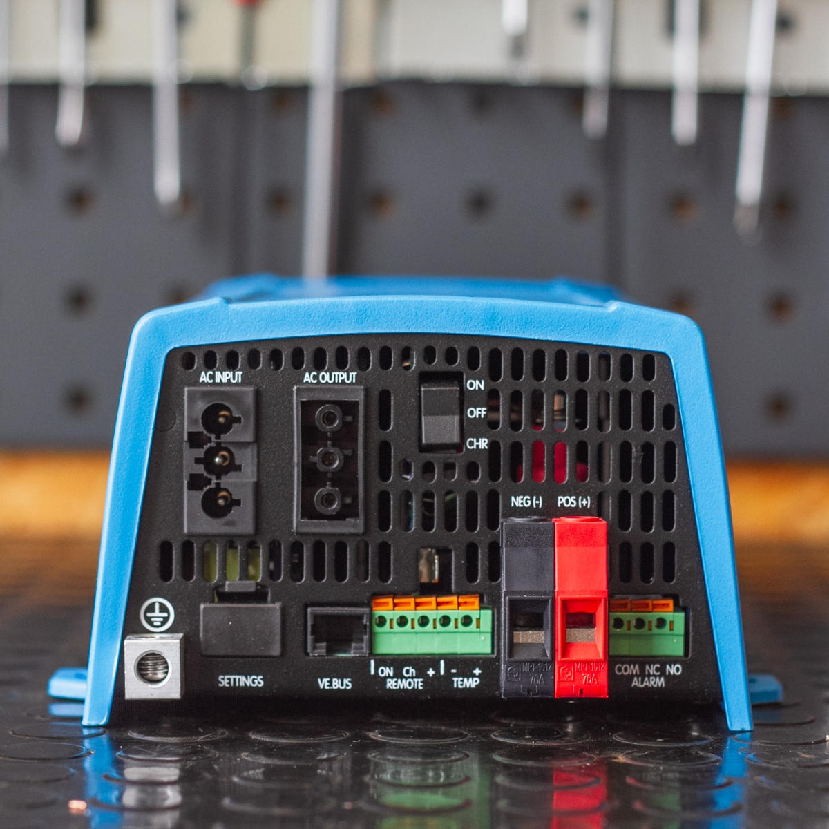 The blue electronic device, the Victron MultiPlus 500VA 12V Inverter/Charger, features various ports and switches labeled AC input, AC output, ON, OFF, NEG, POS, and settings.