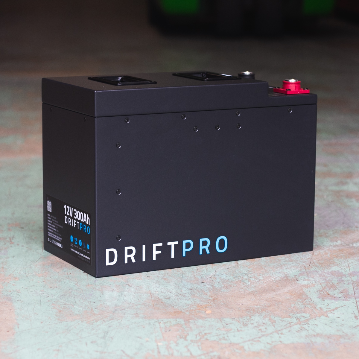 A black Fogstar Drift PRO 300Ah - 12V lithium leisure battery with specifications "12V 300Ah" rests on a concrete floor.