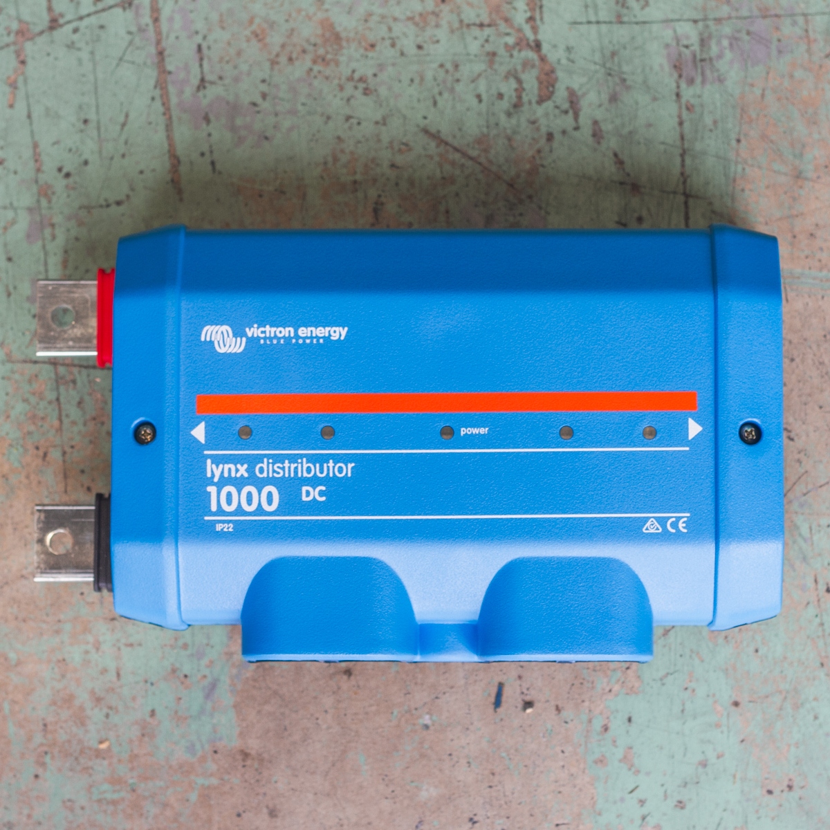 A blue "Victron Energy" Lynx Distributor 1000 DC device with red and black terminals, featuring the Victron Lynx Distributor 1000A Busbar, rests on a worn green surface.