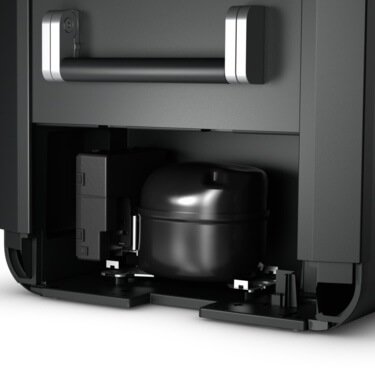 Close-up of the internal components of a black, open refrigerator bottom panel, revealing the compressor and other parts of a Dometic CFX3 55 - Compressor Cool Box - 55L Portable Fridge Freezer.