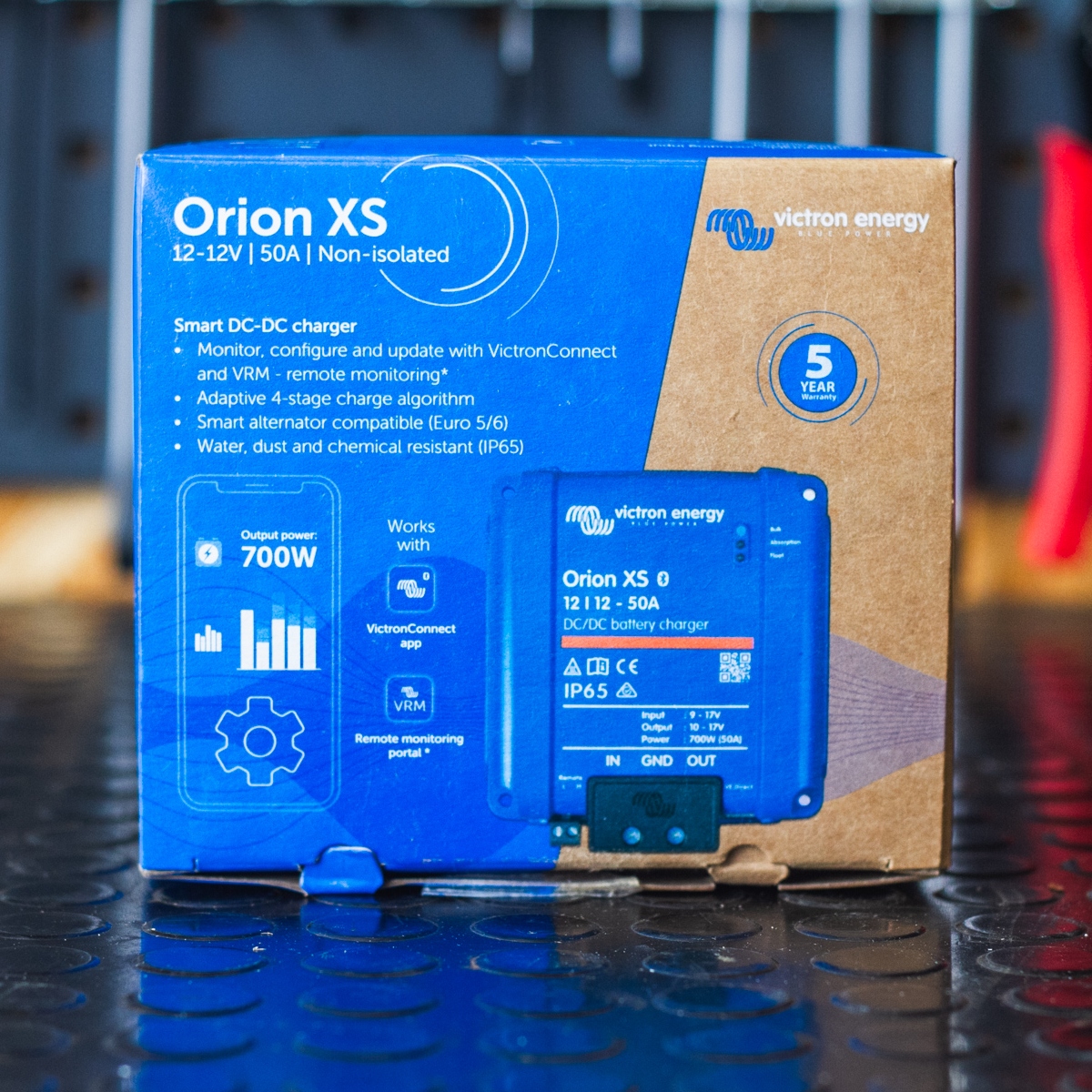A boxed Orion XS 12/12-50A DC-DC Battery Charger - Victron Non-Isolated Smart BuckBoost is elegantly placed on a reflective dark surface.