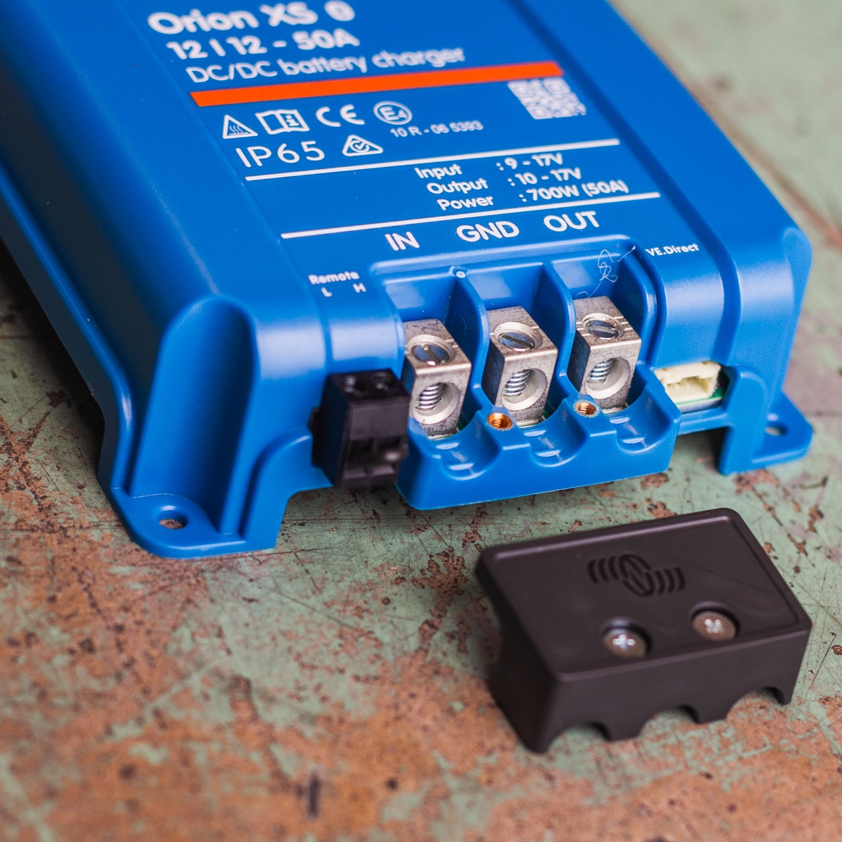 Close-up of a blue Orion-Tr Smart DC/DC battery charger on a workbench, featuring connectors and terminals, showcasing the reliable performance of the Orion XS 12/12-50A Victron Non-Isolated Smart BuckBoost.