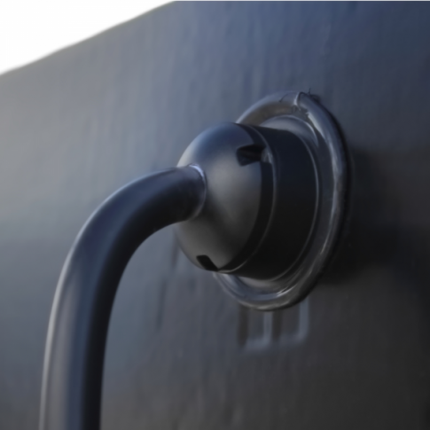 Close-up of a black cable plugged into a round, black socket on a dark surface, ready to connect to a 100W Black Semi-Flexible Solar Panel (Rear Junction Box).