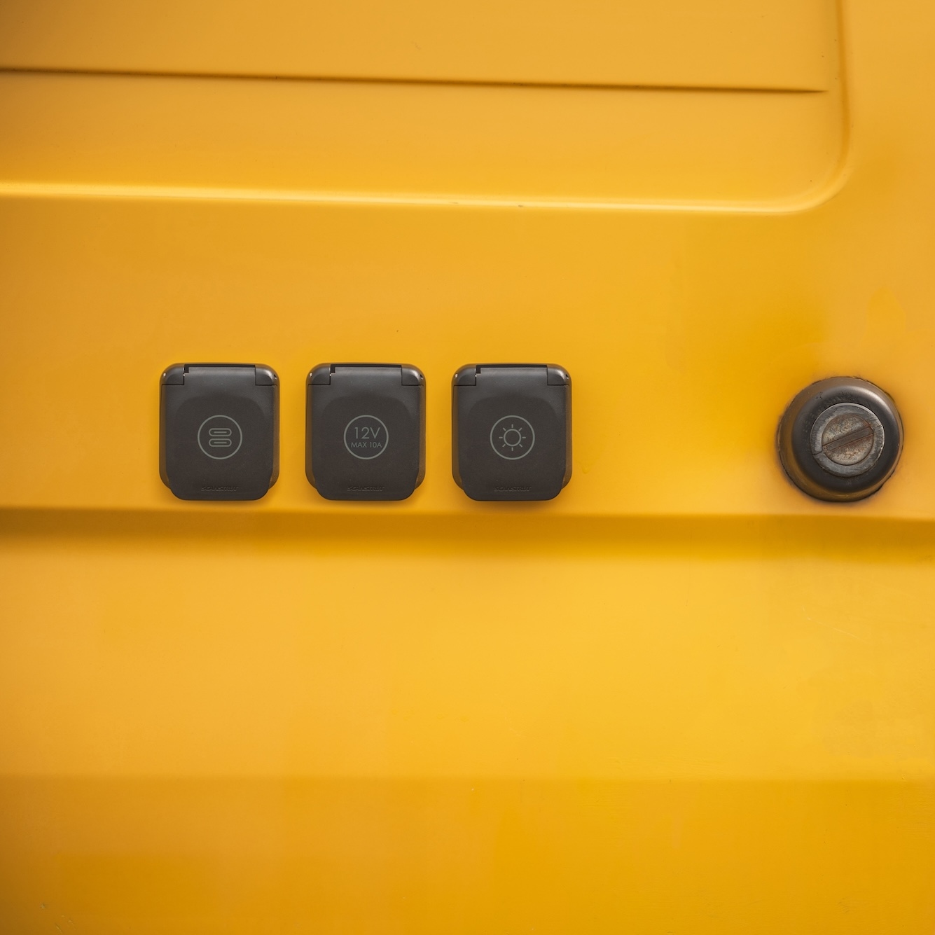 Three black electrical outlets and a Scanstrut Ventura - Cold Water Outlet are placed on a yellow surface next to a round metal socket.