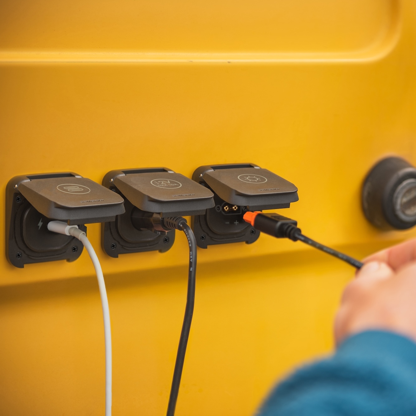 Three charging ports with cables plugged into a yellow surface; a hand connects one cable on the right, showcasing the Scanstrut Ventura - XT60 Solar Connection for efficient, reliable charging.