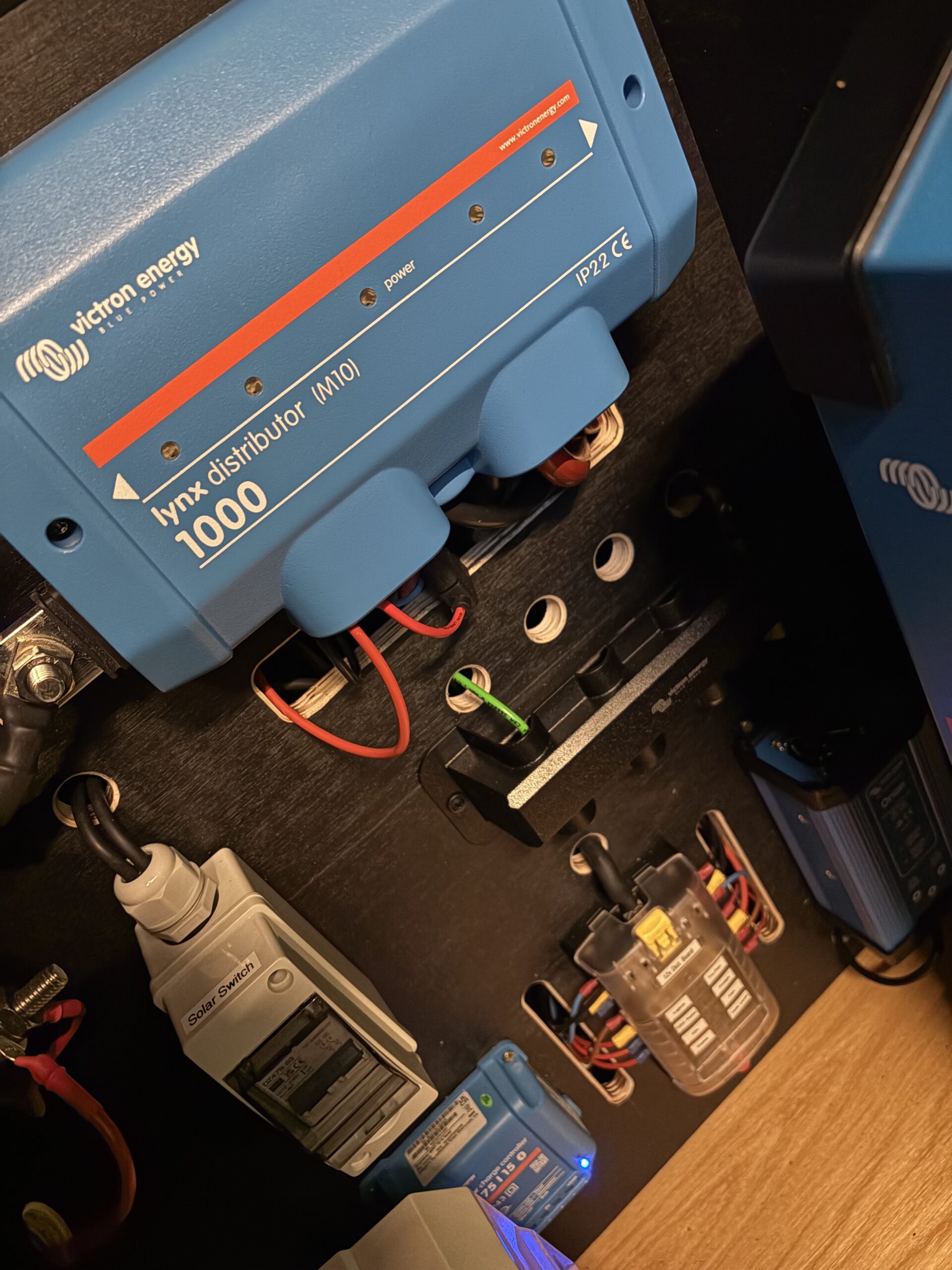 Blue Victron Energy Lynx Distributor 1000 with connected wires and electrical components mounted on a black panel, expertly assembled by Sam Kidd.