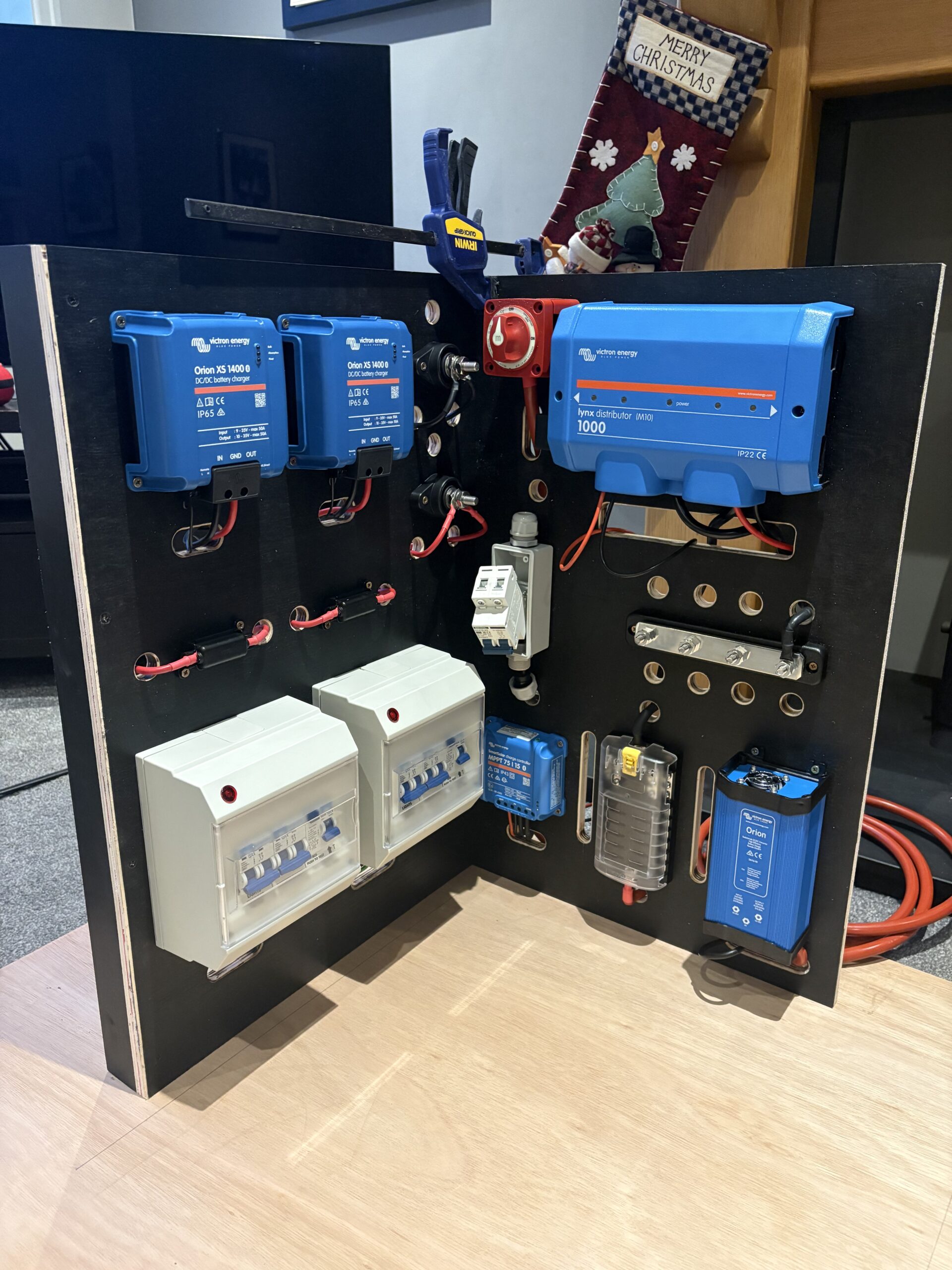 Electrical control panel with blue devices, circuit breakers, and wiring mounted on a black board, expertly assembled by Sam Kidd.