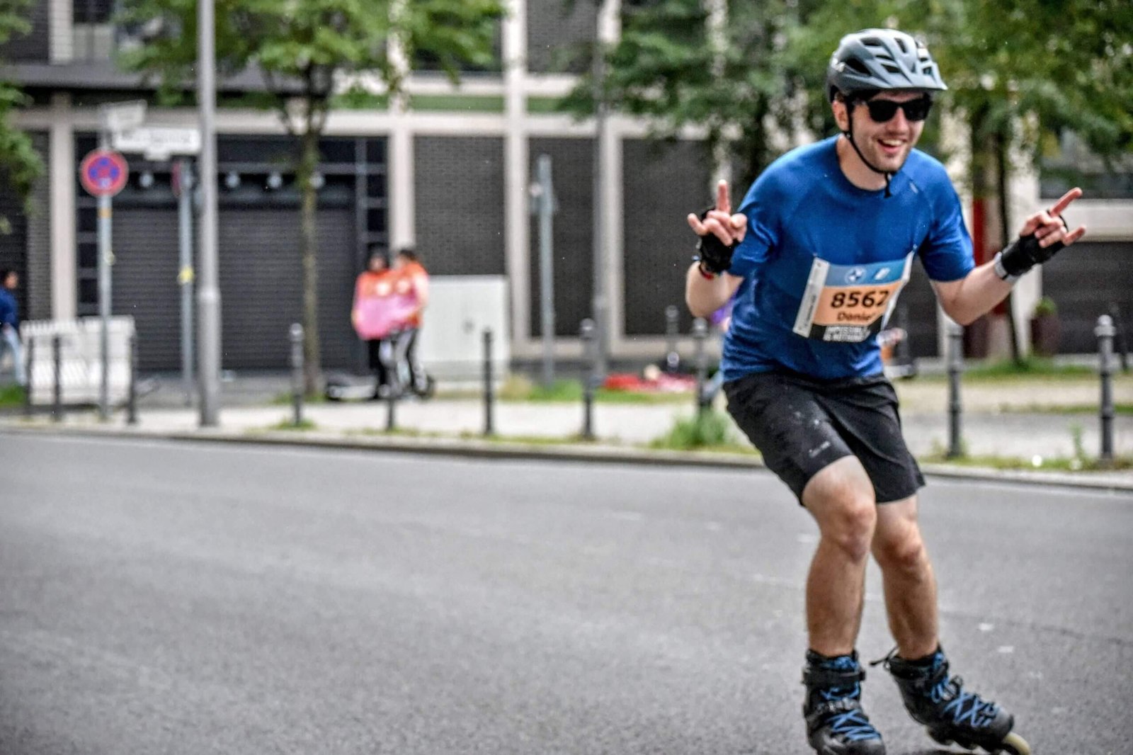 Dan wering a helmet, sunglasses and wrist guards whilst inline skating on a road through a city during race