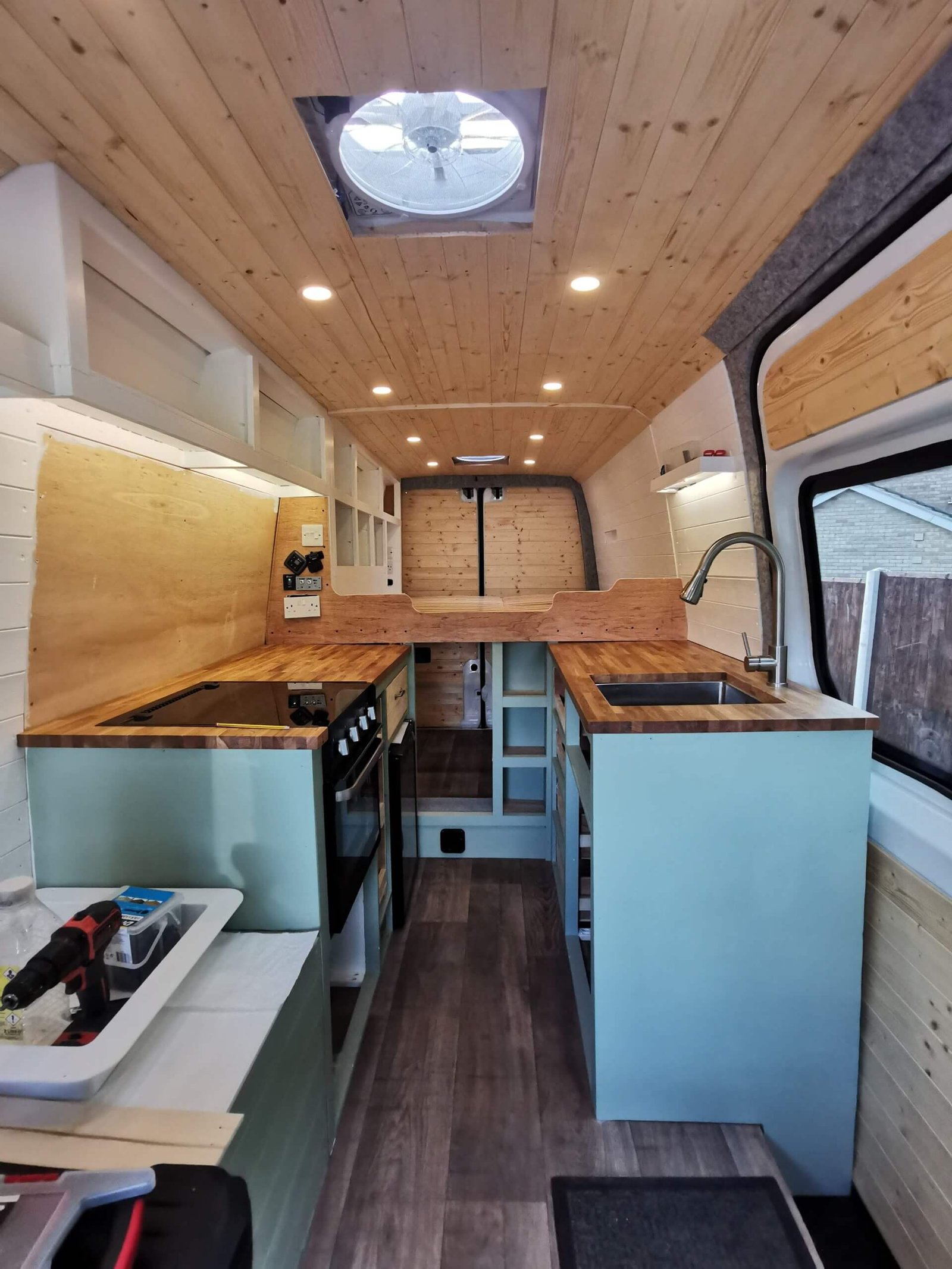 The finished light blue, brown and white interior of Dan's self converted van looking towards the back doors with kitchen counter on both sides and a bed in the rear