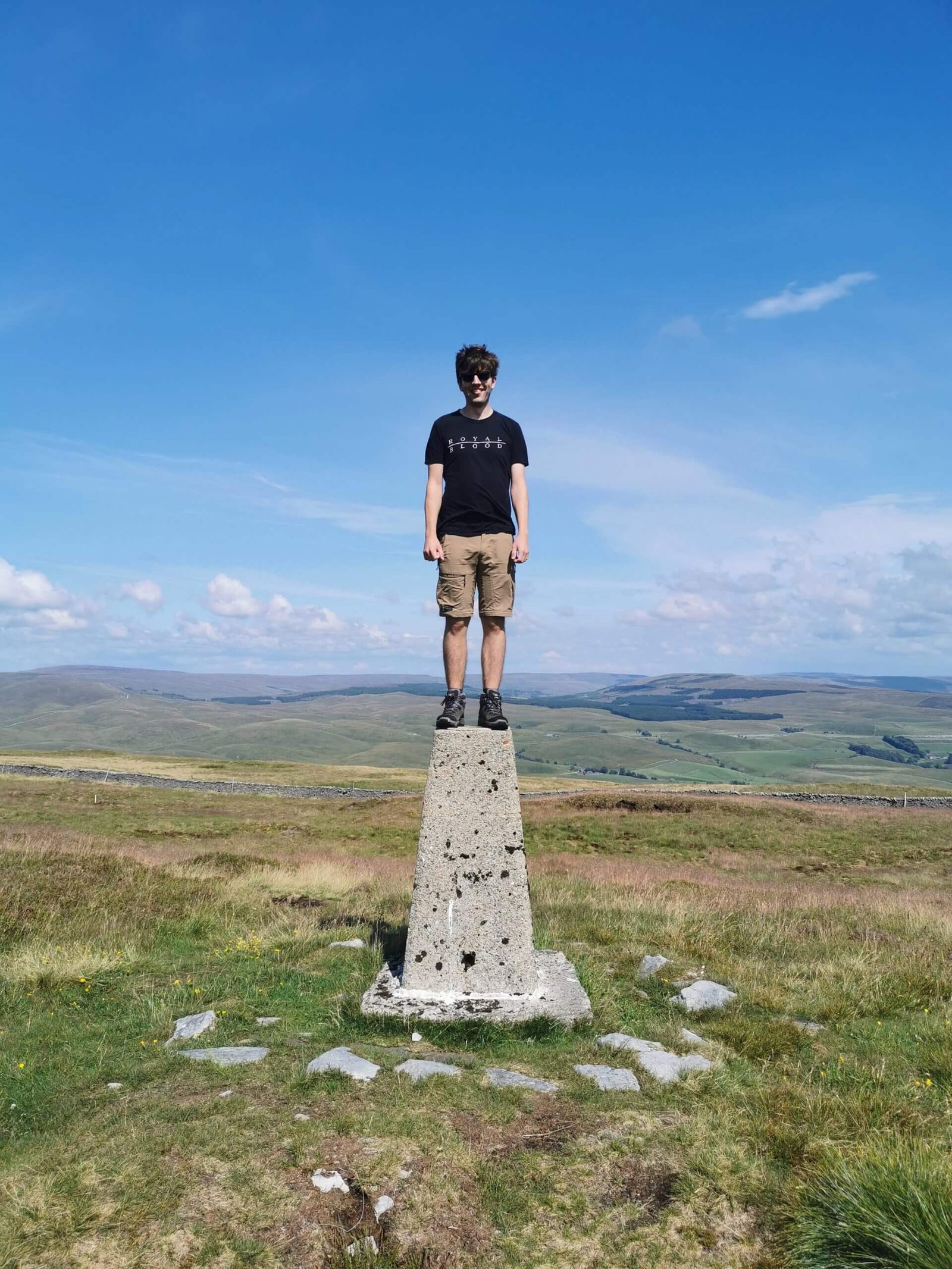 Dan standing on top of a peak marker with green hills in the background