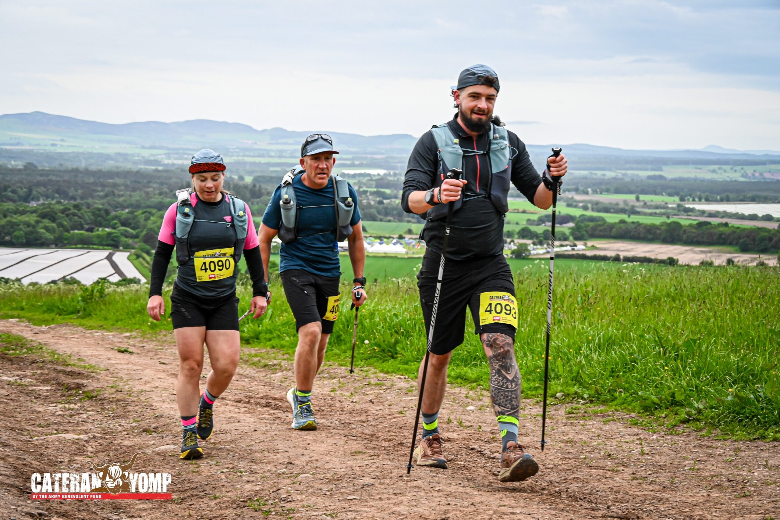 Huey and two of his teammates hiking through a green landscape wearing yellow numbered bibs and holding hiking poles